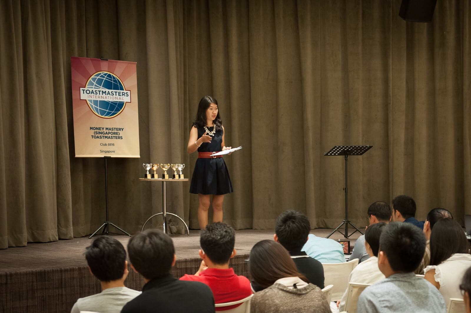 A speaker presenting on stage at a Toastmasters event to a seated audience